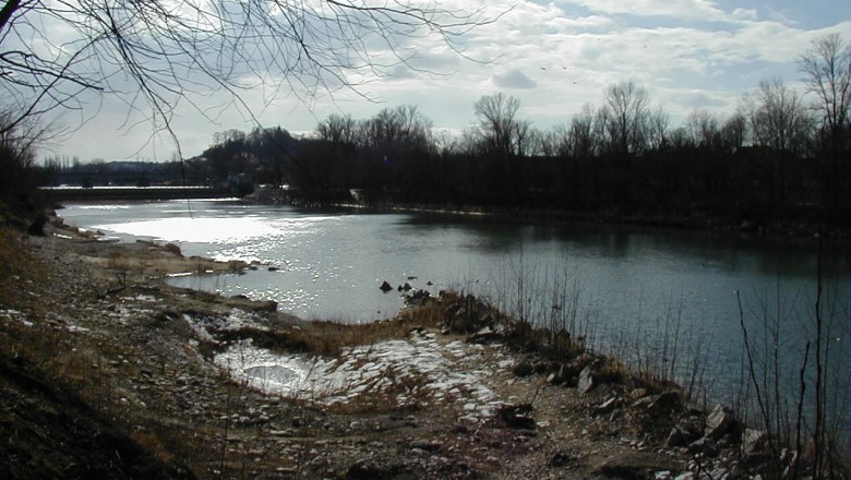A calm river with bare trees on the banks under a cloudy sky.
