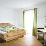 Bright room with wooden bed, green and white striped bed linen, table with vase and plant, green curtains.