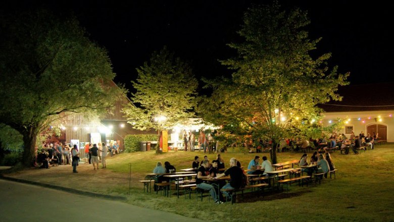 Night shot of an illuminated outdoor event area with people at tables and colorful lights.