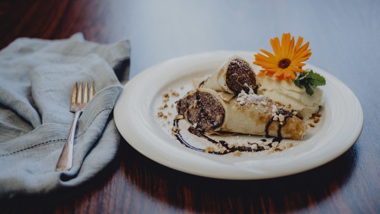Dessert plate with filled pancakes, cream, chocolate sauce and flower.