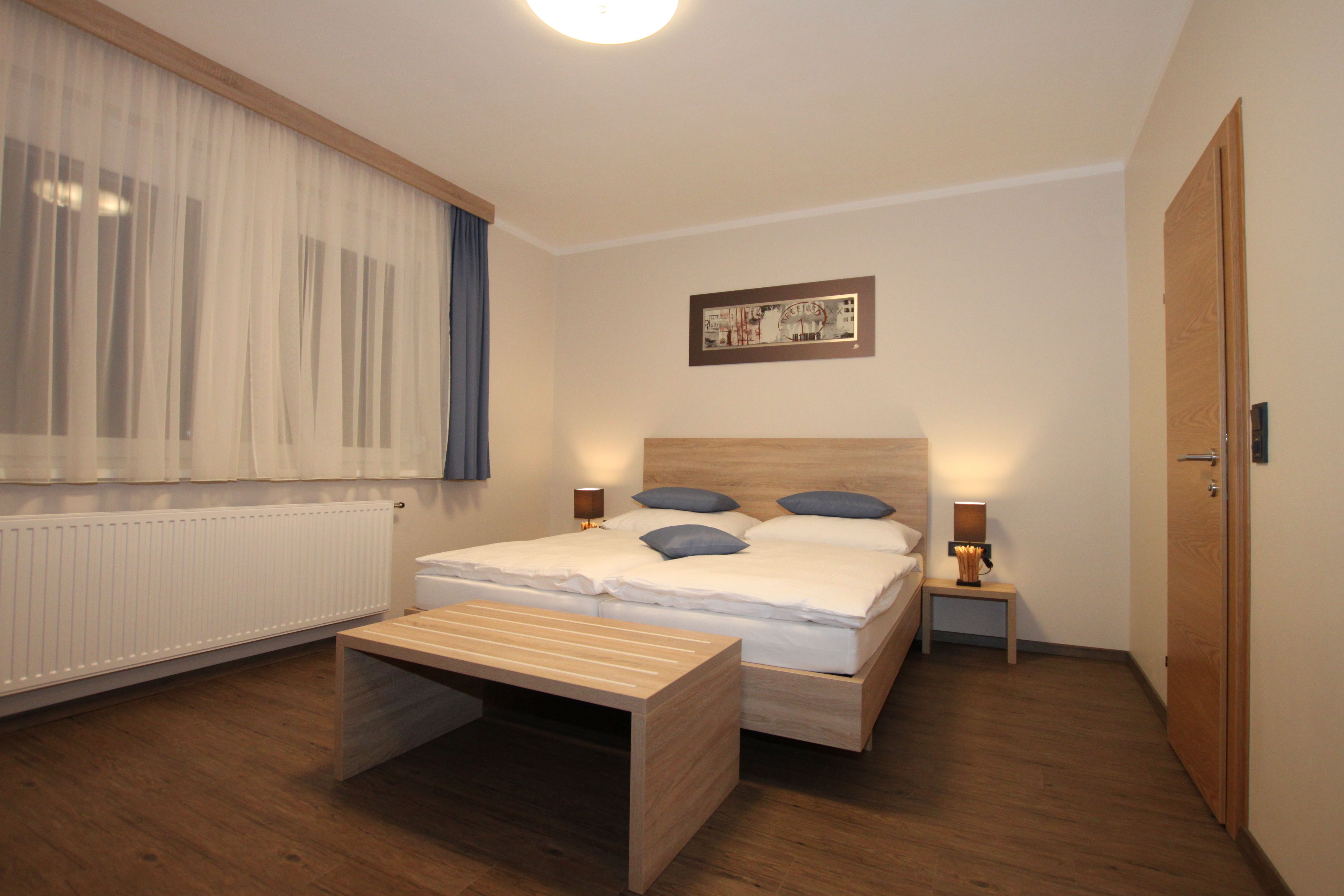 A simply furnished room with a double bed, wooden furniture and curtains.