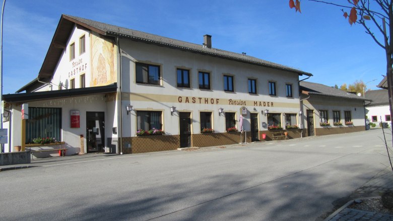 Gasthof Mader on a quiet street with flower boxes in bloom and a blue sky.
