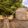 Wooden sauna with two chairs and table on a wooden terrace surrounded by greenery.