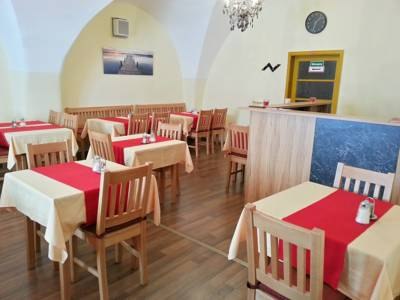 A breakfast room with wooden tables and red table runners, decorated with a picture on the wall and a chandelier on the ceiling.