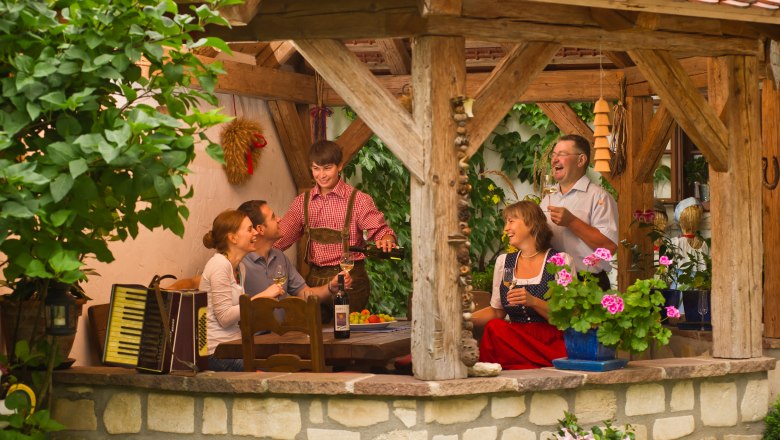 A group of people sit in a covered, rustic pavilion and enjoy wine and company.