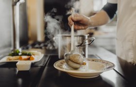 One person ladles soup with a dumpling from a pot into a plate.