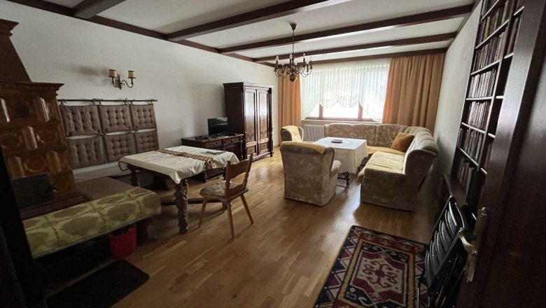 Living room with wooden floor, sofa, table, cupboard and fireplace.