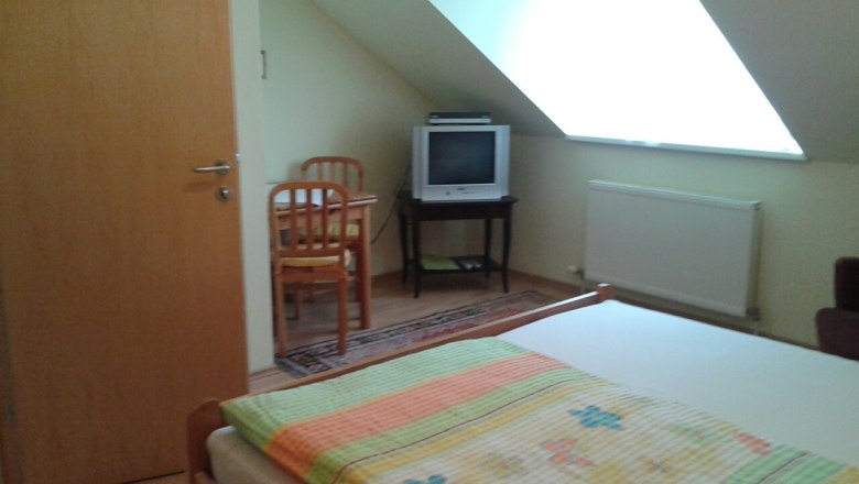 A simply furnished room with a bed, TV and table under a sloping roof.