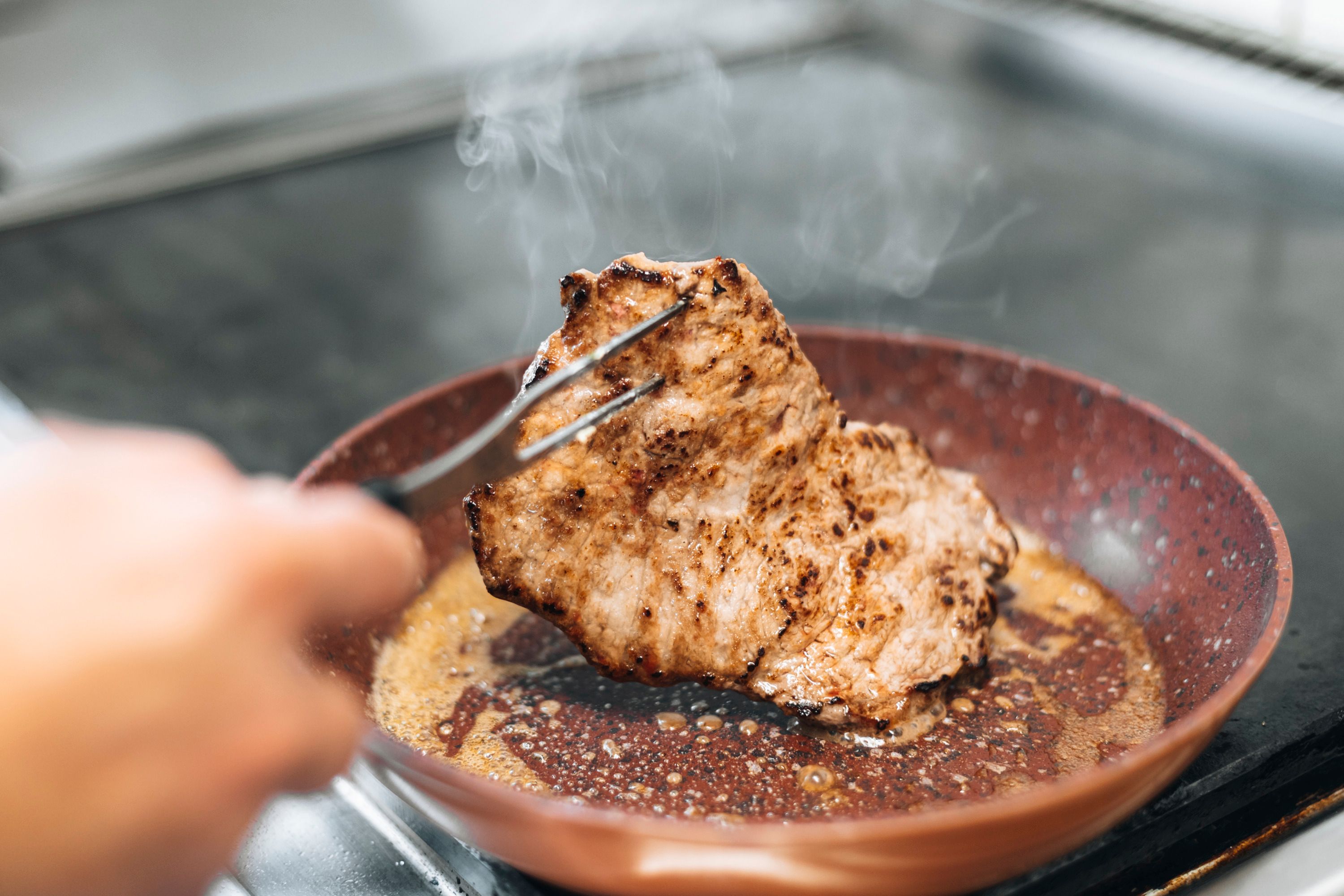 A piece of meat is fried in a pan.