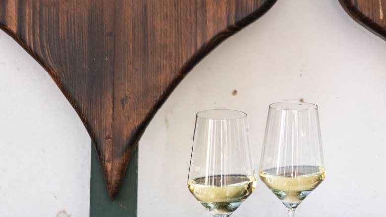 Two wine glasses with white wine on a wooden table in front of a heart-shaped wooden decoration.