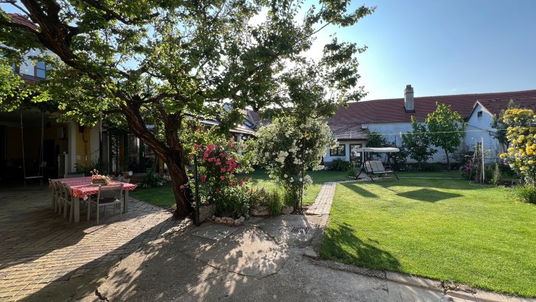 A sunny garden with table, chairs, flowers and a swinging bench.