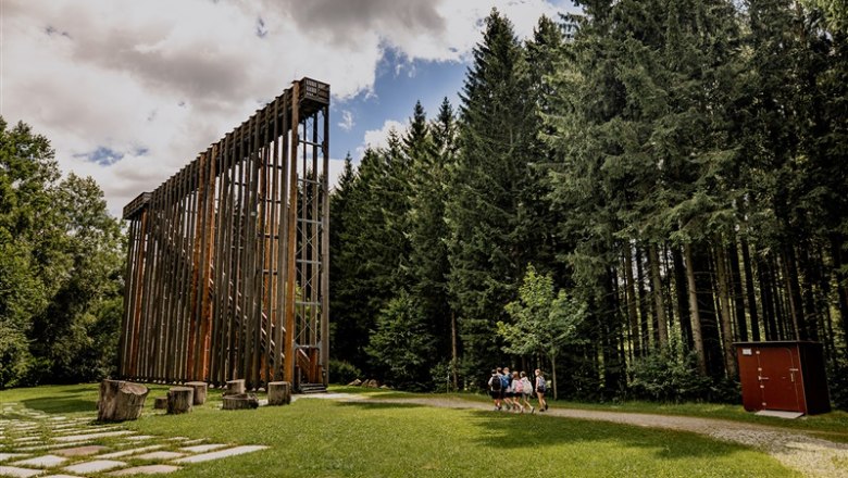Wooden construction in the forest with people on a meadow.