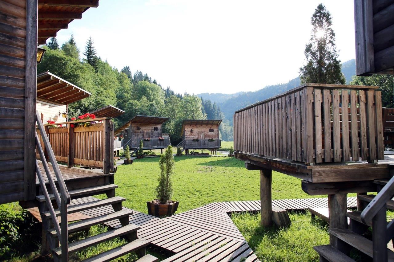 Wooden huts in a green valley with forest in the background.