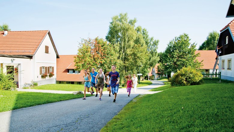 Group of people walking on a path in a vacation village with red roofs and green surroundings.
