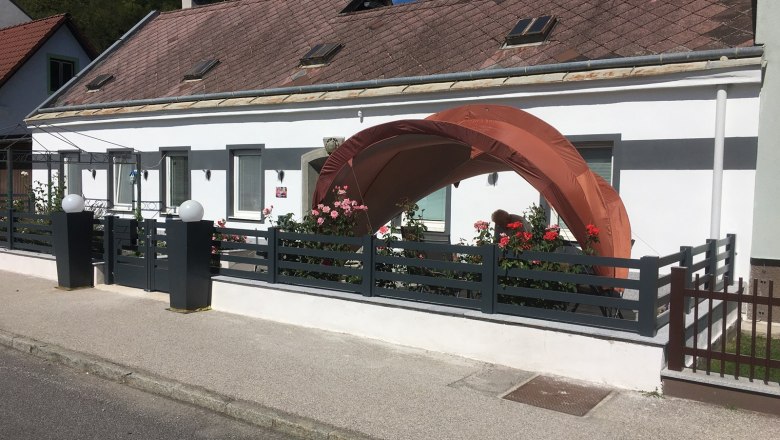 A white house with a small garden and an orange pavilion in front of the door.
