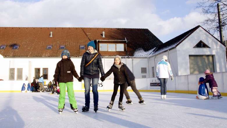 People skating on an artificial ice rink in front of a building.