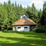 A round house with a pyramid roof in the middle of a forest.