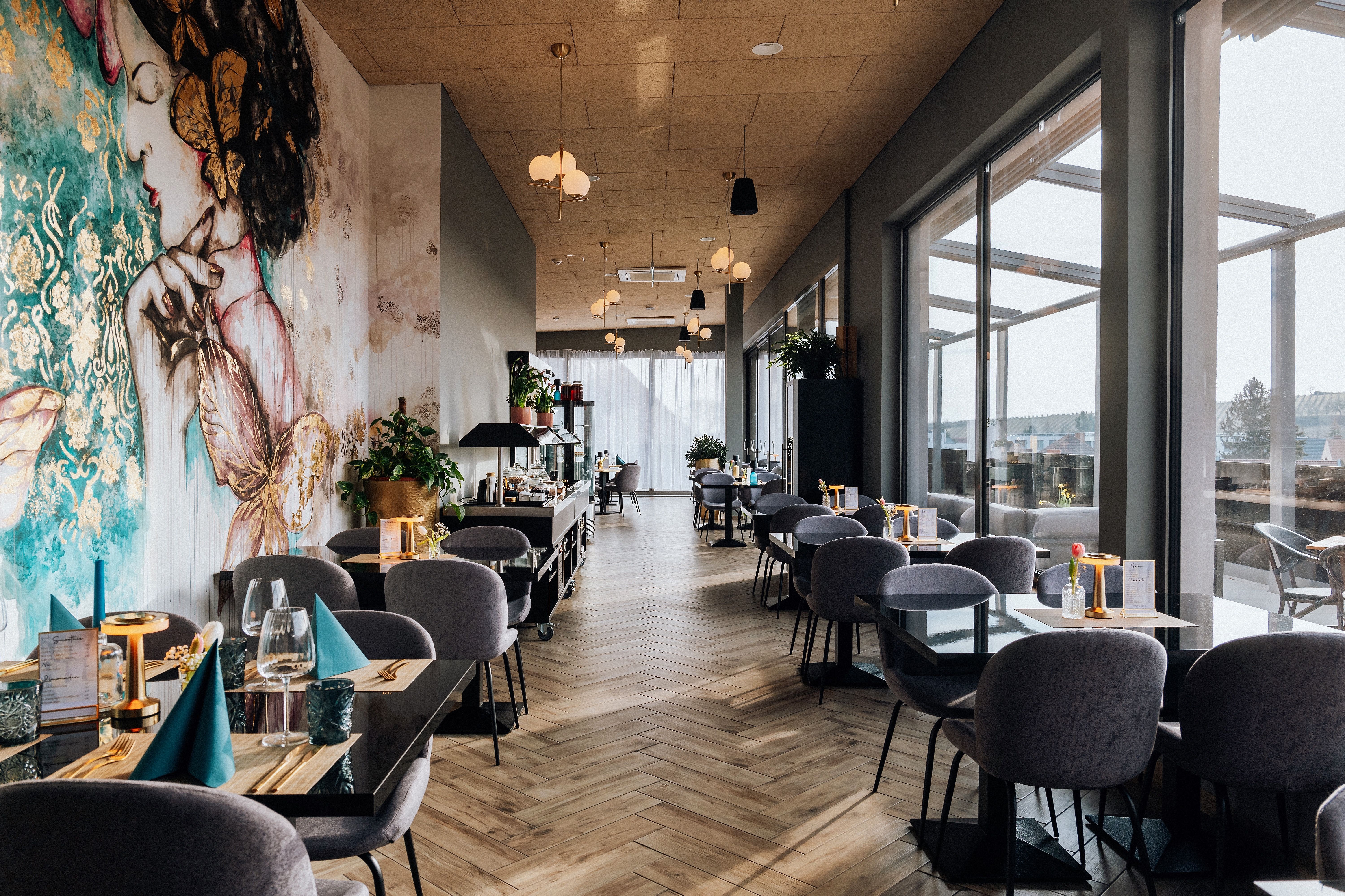 Interior view of a stylish restaurant with large windows and artistic murals.