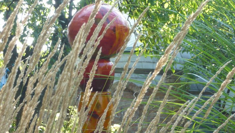 Colorful sculpture in the garden behind grasses and plants.