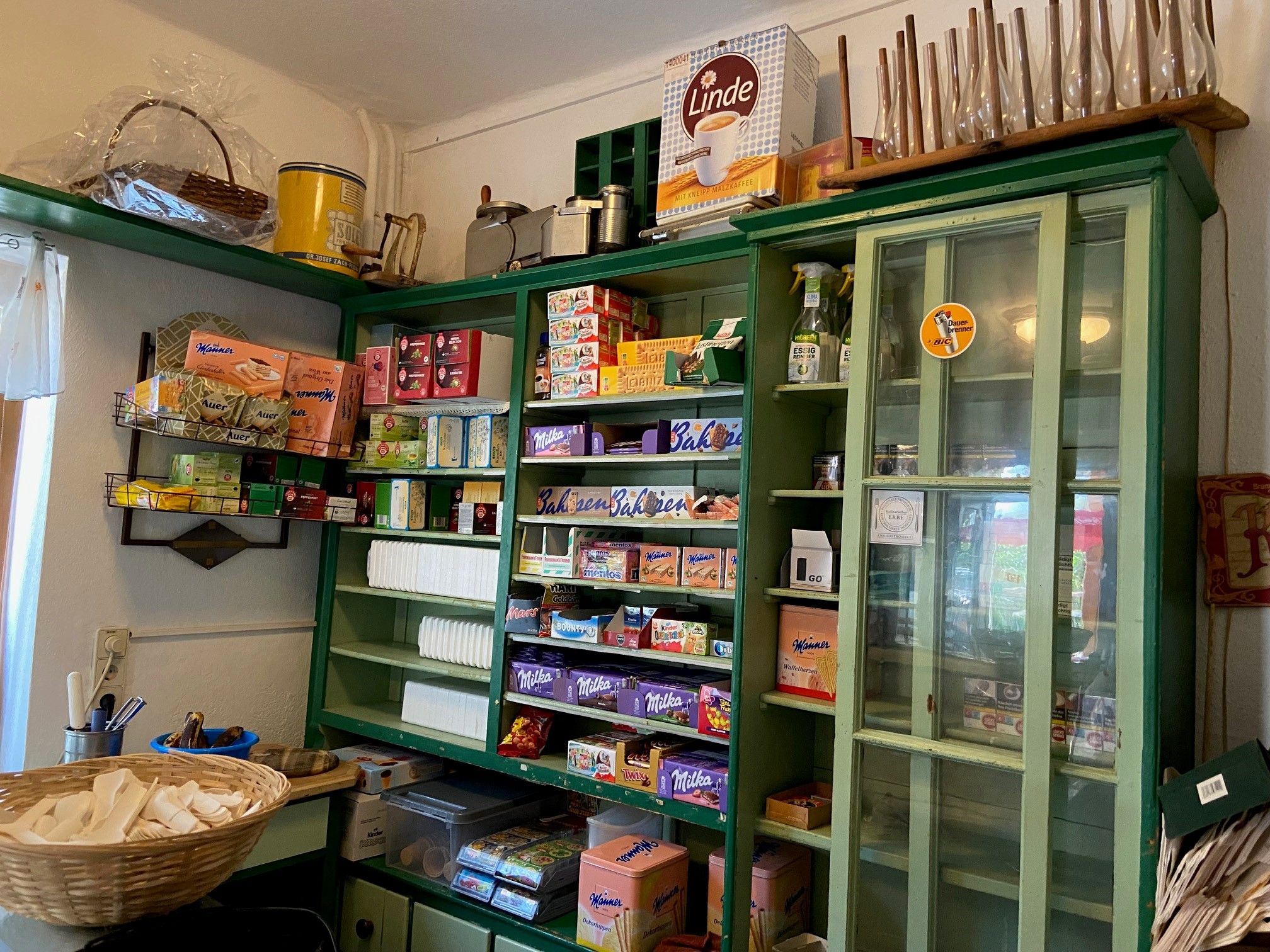 A traditional store with green shelves filled with various groceries and household goods.