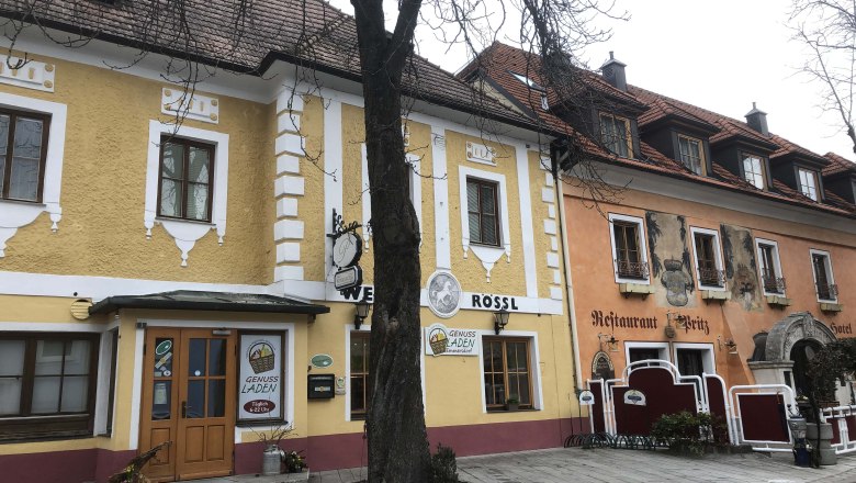 Exterior view of a yellow building with restaurant and hotel, tree in the foreground.