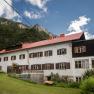 A traditional inn with a red roof in front of a wooded mountainside.