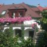 A guest house with a balcony full of pink flowers, surrounded by green vegetation.