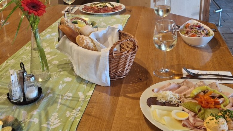 A laid table with a platter of cold meats and cheese, bread basket, salad and wine glasses.