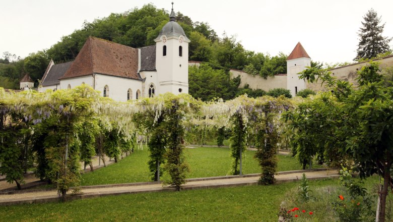 View of a historic charterhouse with garden and pergola.
