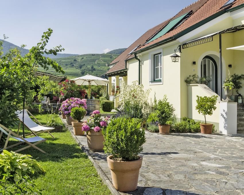 An idyllic country house with a well-tended garden, flowering plants and sun loungers under a sunny sky.