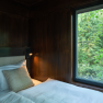 Interior view of a tree house with a bed and a window overlooking the forest.