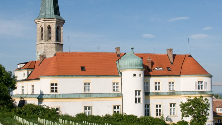 Gumpoldskirchen Castle with its red roof and tower, surrounded by vineyards under a blue sky.