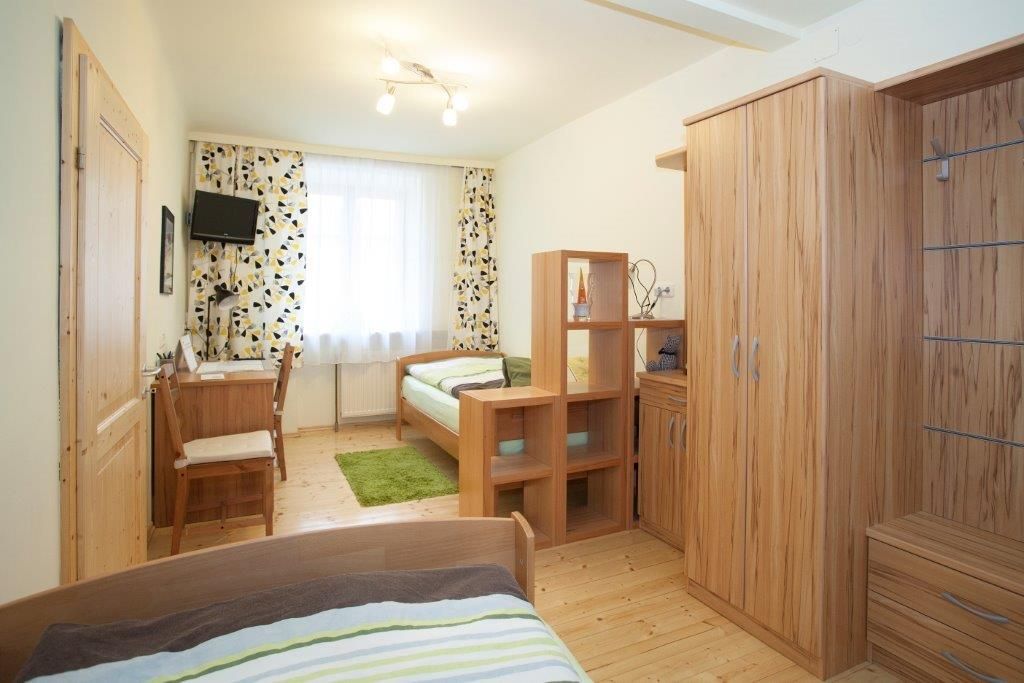 A bright bedroom with wooden furniture, two beds, a desk and a small TV on the wall.