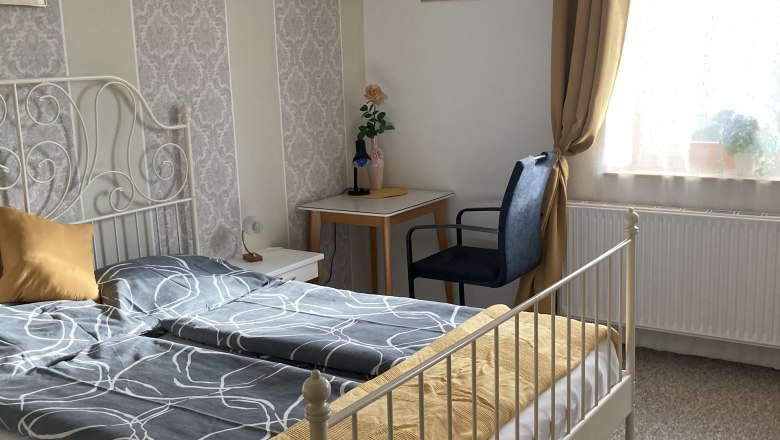 Cozy bedroom with double bed, yellow curtains and decorative wallpaper.