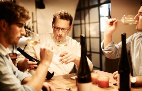Three men tasting wine at a table with bottles of wine.