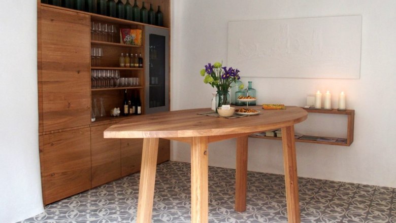 A stylish tasting room with a wooden table, shelves with bottles and glasses, flowers and candles.