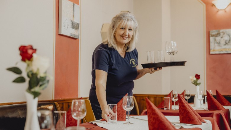 Woman sets table in a restaurant with glasses and red napkins.
