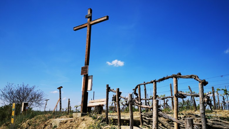 Wooden cross on a hill with vines and blue sky in the background.