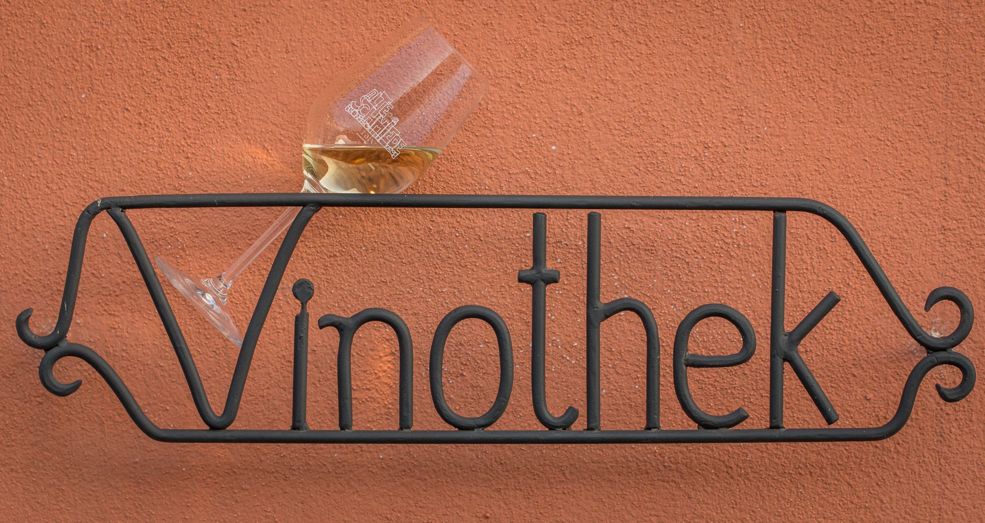 Metal sign with the inscription 'Vinothek' and a wine glass on a red wall.