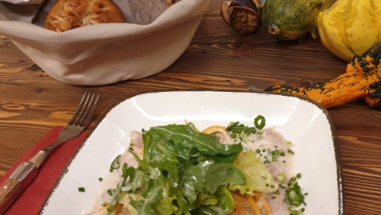 A plate of pasta and salad on a wooden table, with a bread basket and ornamental pumpkins next to it.
