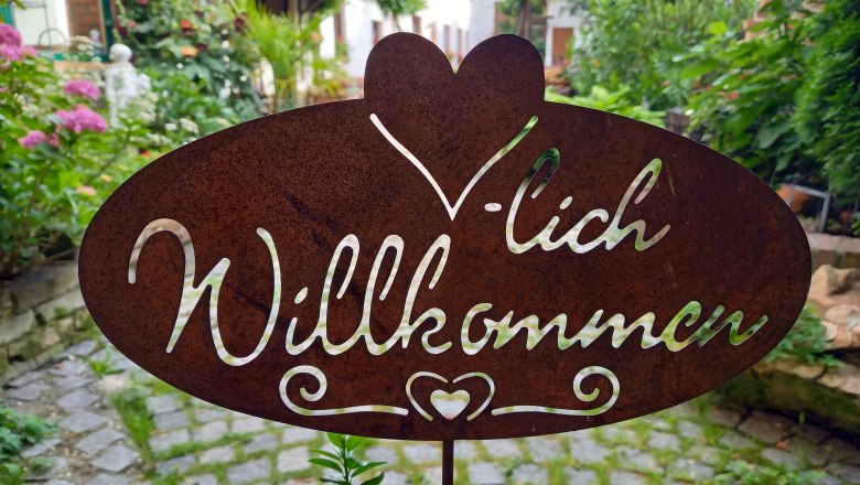 Metal sign with the inscription 'Welcome' in a garden.