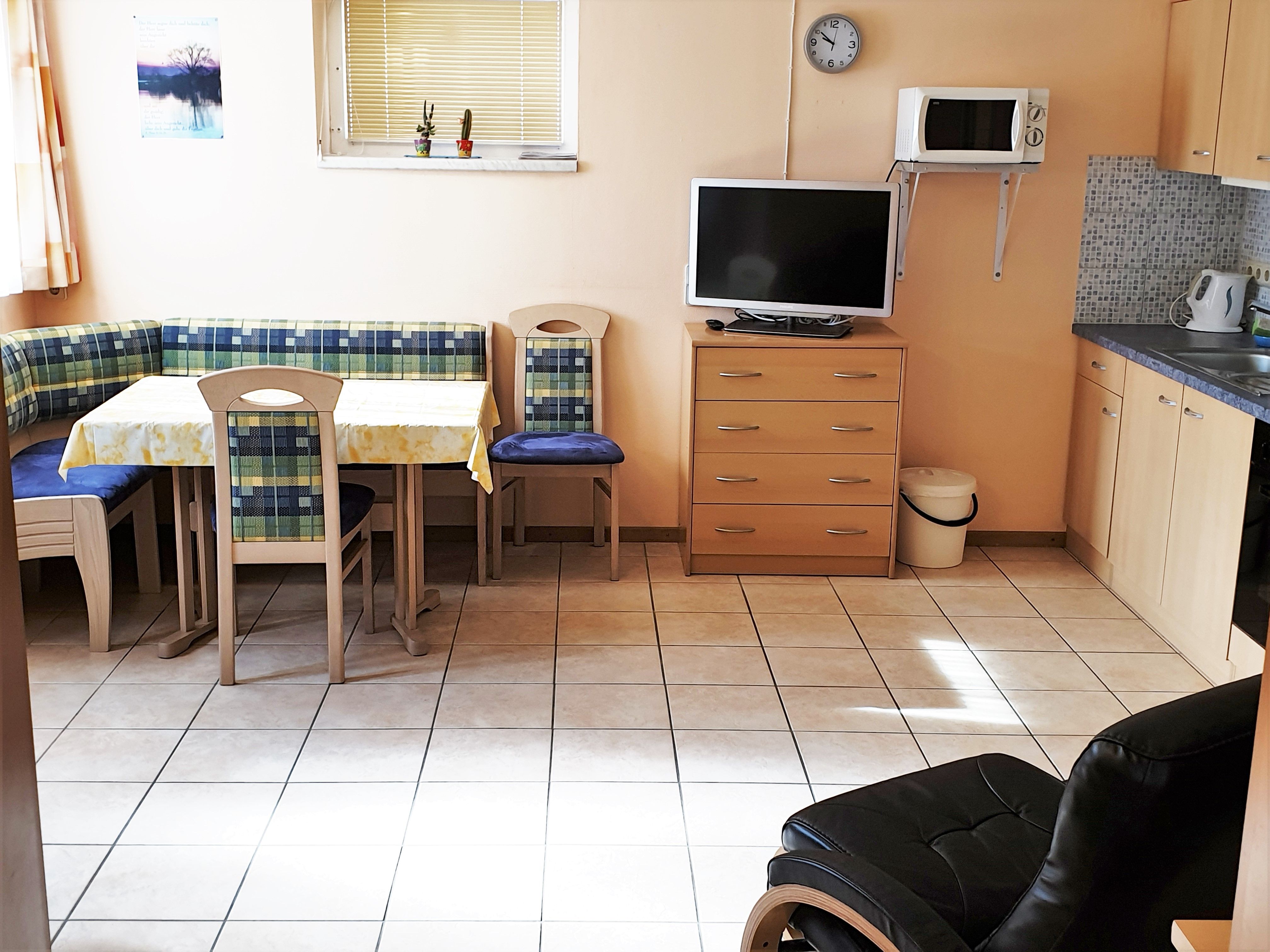 Kitchen with corner bench, table, chairs, TV, microwave and cupboards.