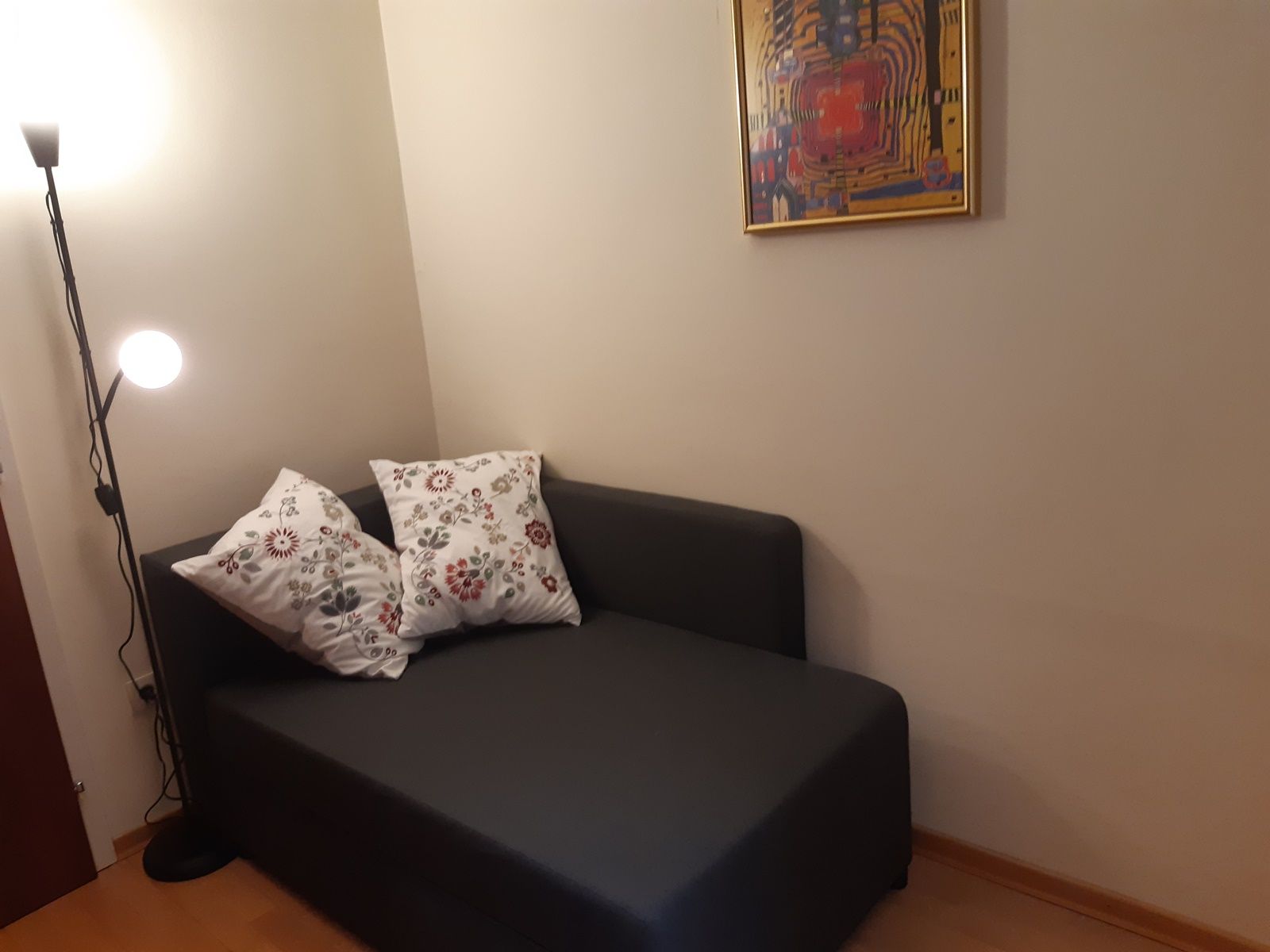 Cozy reading corner with grey sofa, two patterned cushions, floor lamp and abstract picture on the wall.