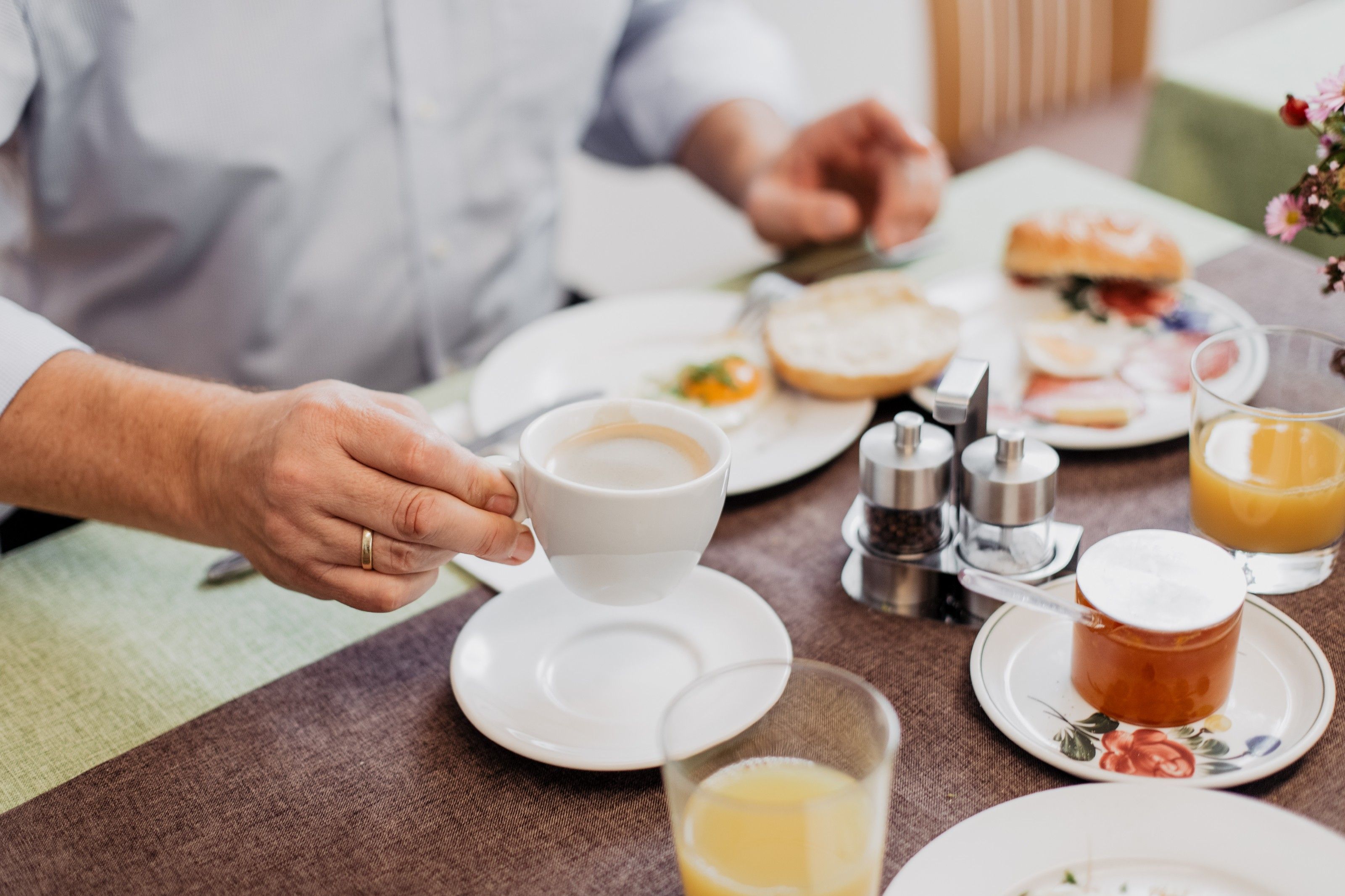 Person holding a cup of coffee over a laid breakfast table.