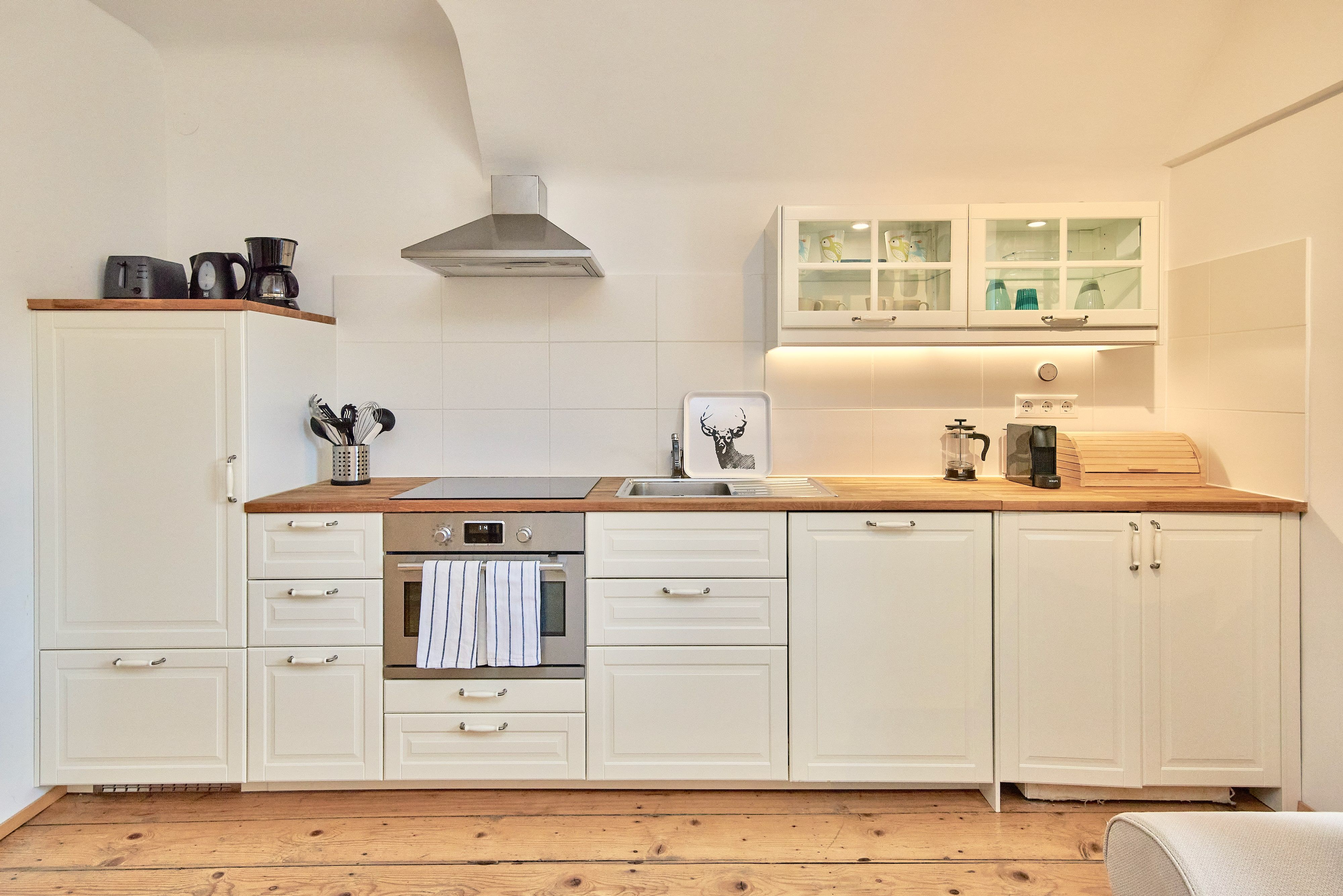 Modern kitchen with white cupboards, wooden worktop, stove, extractor hood and sink.
