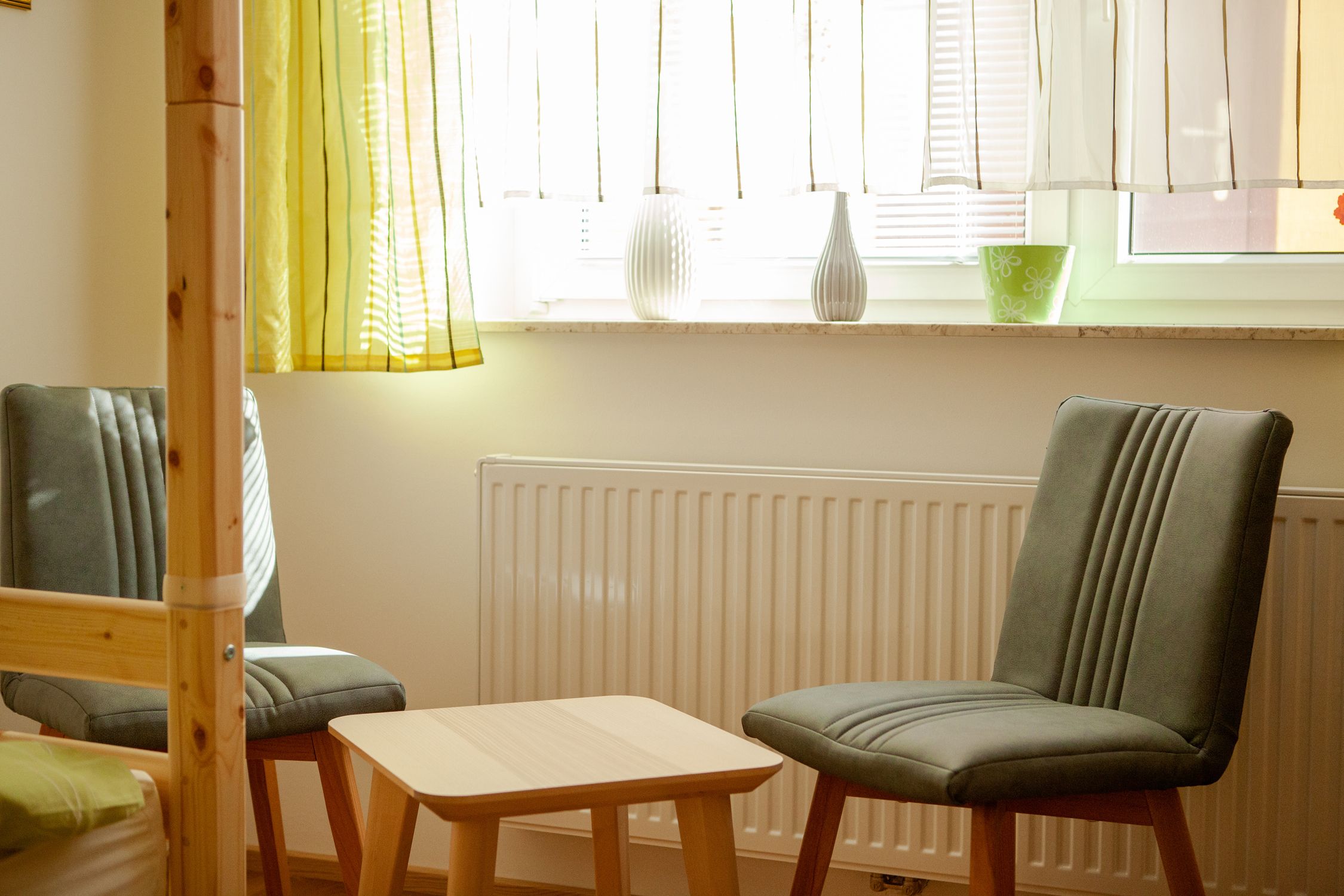 Two gray chairs and a small wooden table in front of a window with curtains in the bedroom.