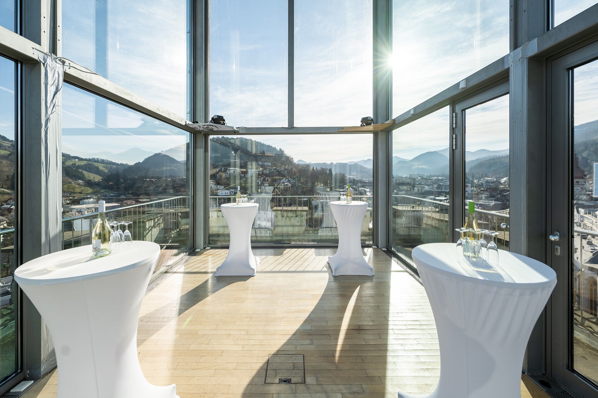 Interior view of a modern glass room with bar tables and mountain views.