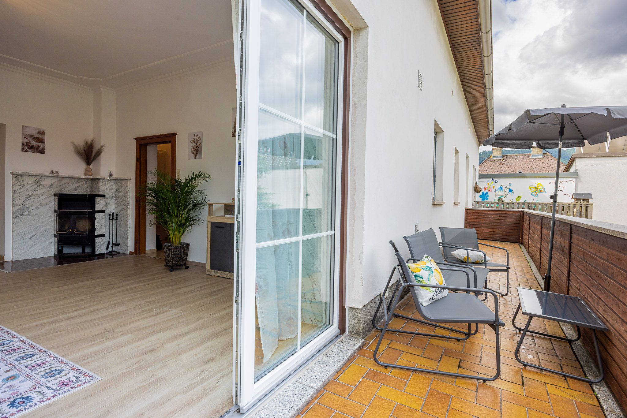 View from a terrace into a living room with fireplace and plants.