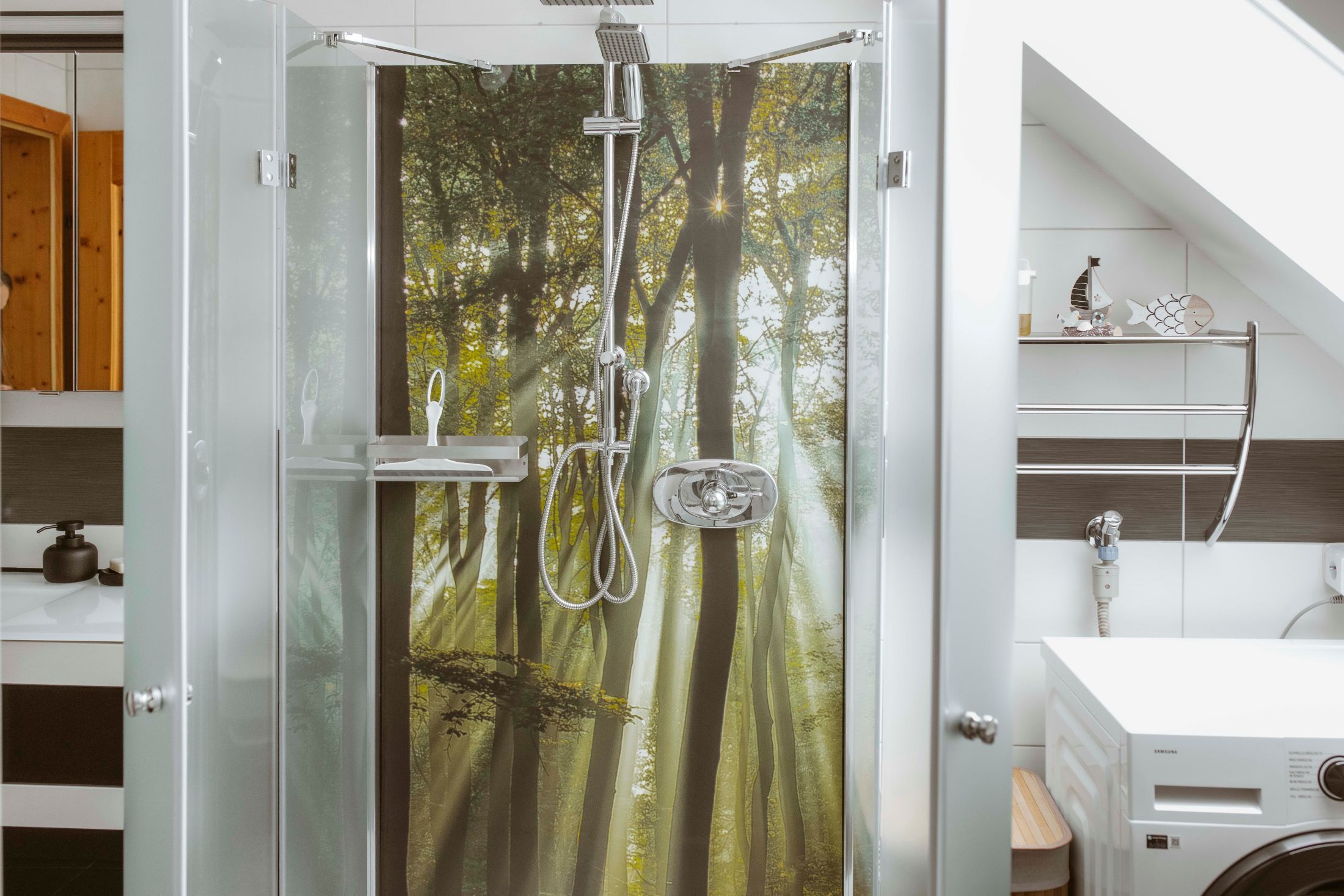 Shower area with forest picture on the back wall, washing machine next to it.
