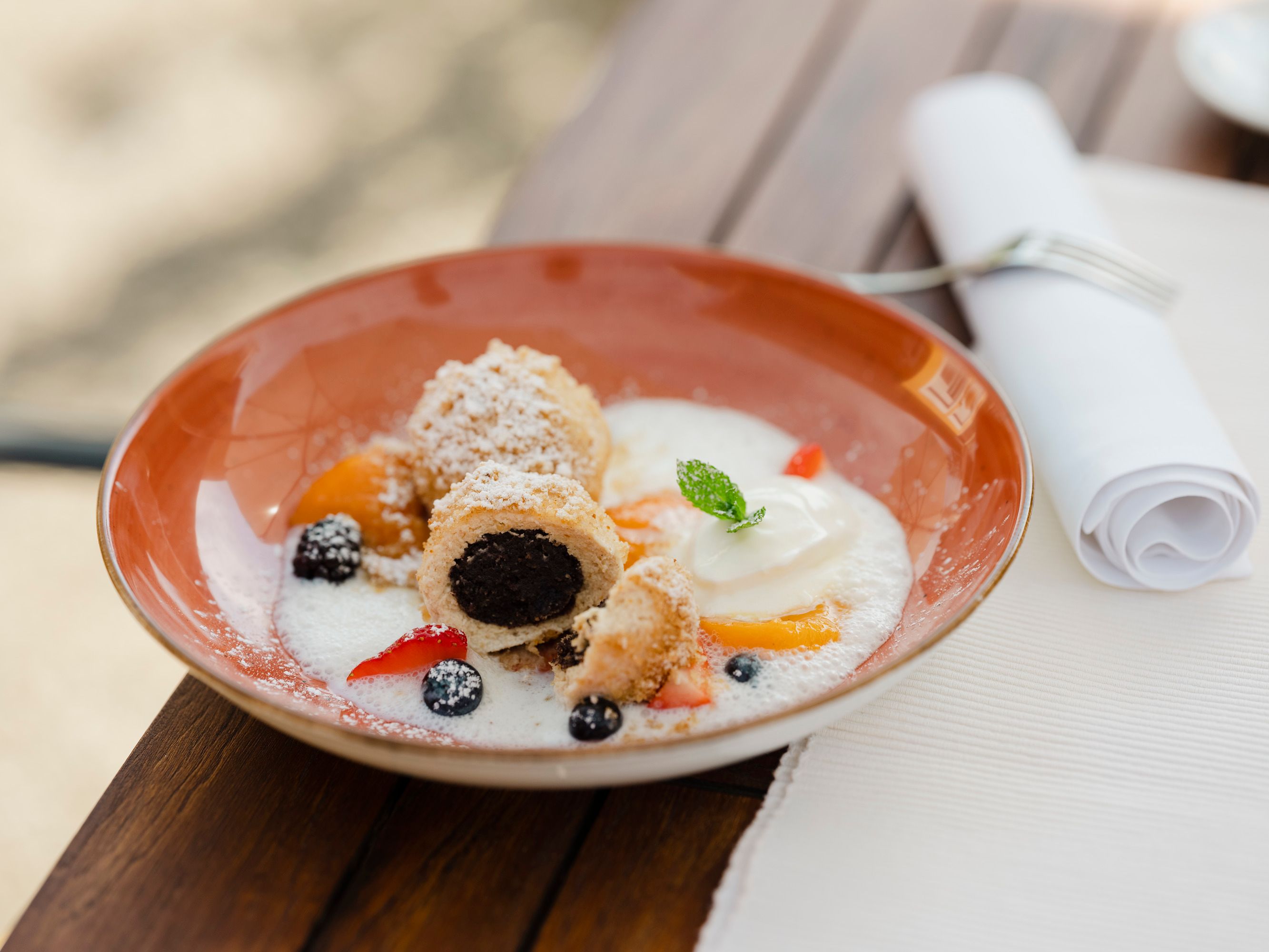 A plate of poppy seed and curd cheese dumplings, garnished with fruit and cream, on a wooden table.